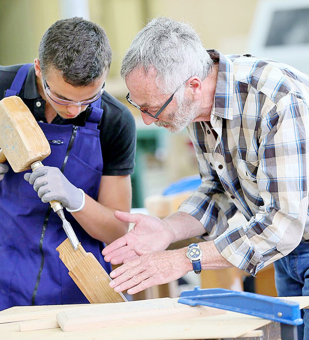 Young apprentice with teacher working on piece of wood Young apprentice with teacher working on piece of wood